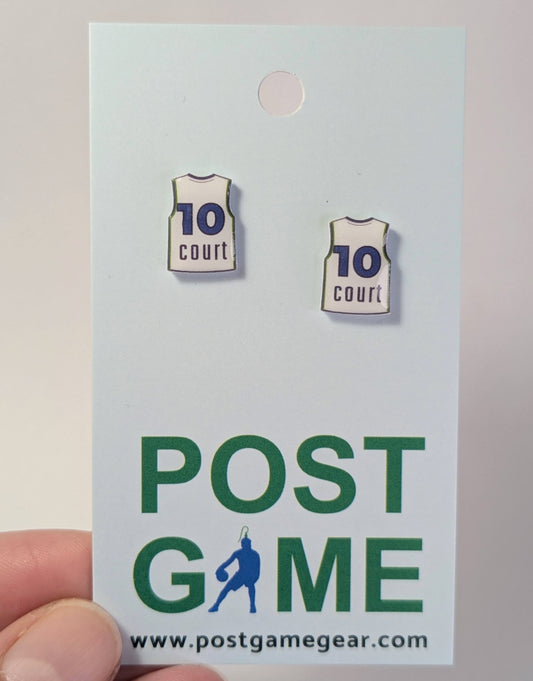 A pair of earrings shaped like basketball jerseys with '10 court' written on them, attached to a white display card featuring the green and blue 'POST GAME' branding. A hand is holding the card at the bottom left.