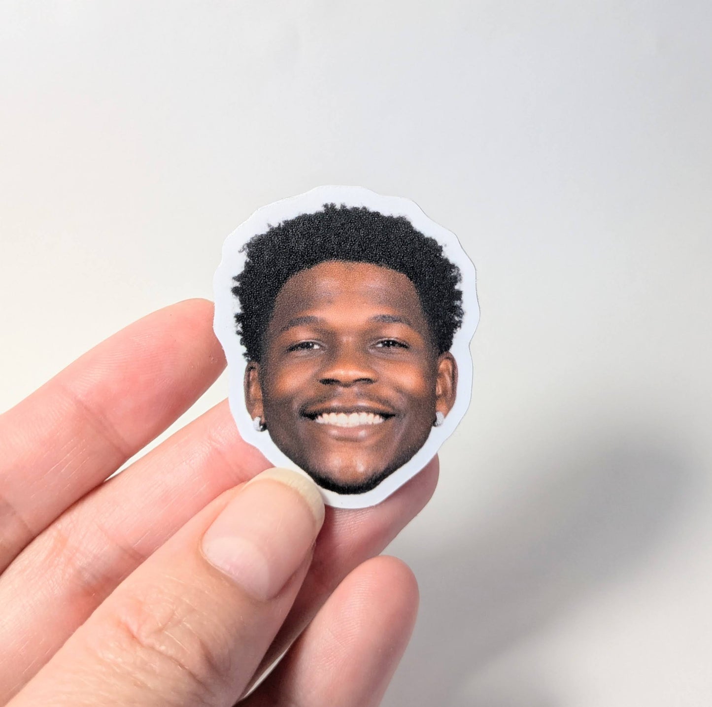 Hand holding a circular sticker with a smiling person's face against a plain background