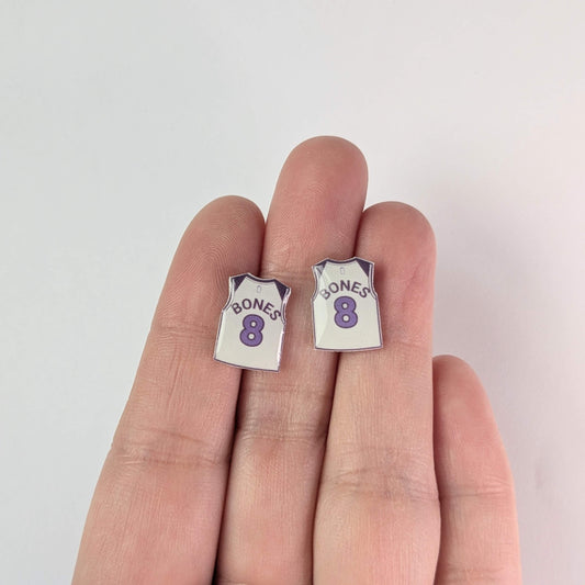 Small earrings shaped like miniature sports jerseys with 'BONES' and number '8' on a hand against a light background
