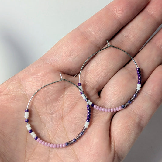 Beaded hoop earrings held in a hand against a neutral background