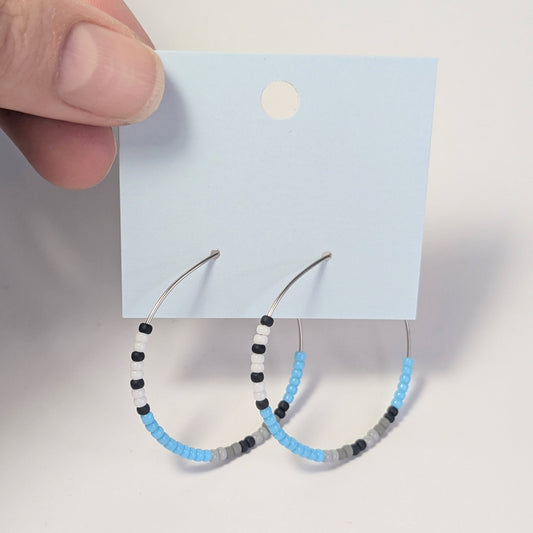 Hoop earrings with blue, black and white beads on a white card held by a hand.