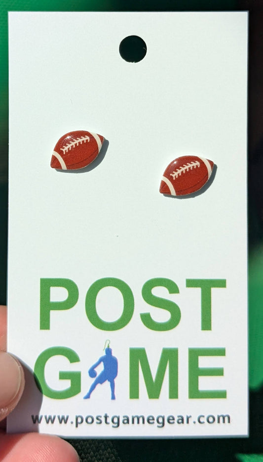 A close-up of a white hang tag with two small football-shaped stud earrings and large green text reading POST GAME, plus the website postgamegear.com.