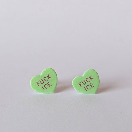 Green heart-shaped earrings with 'FUCK ICE' text on a light gray background