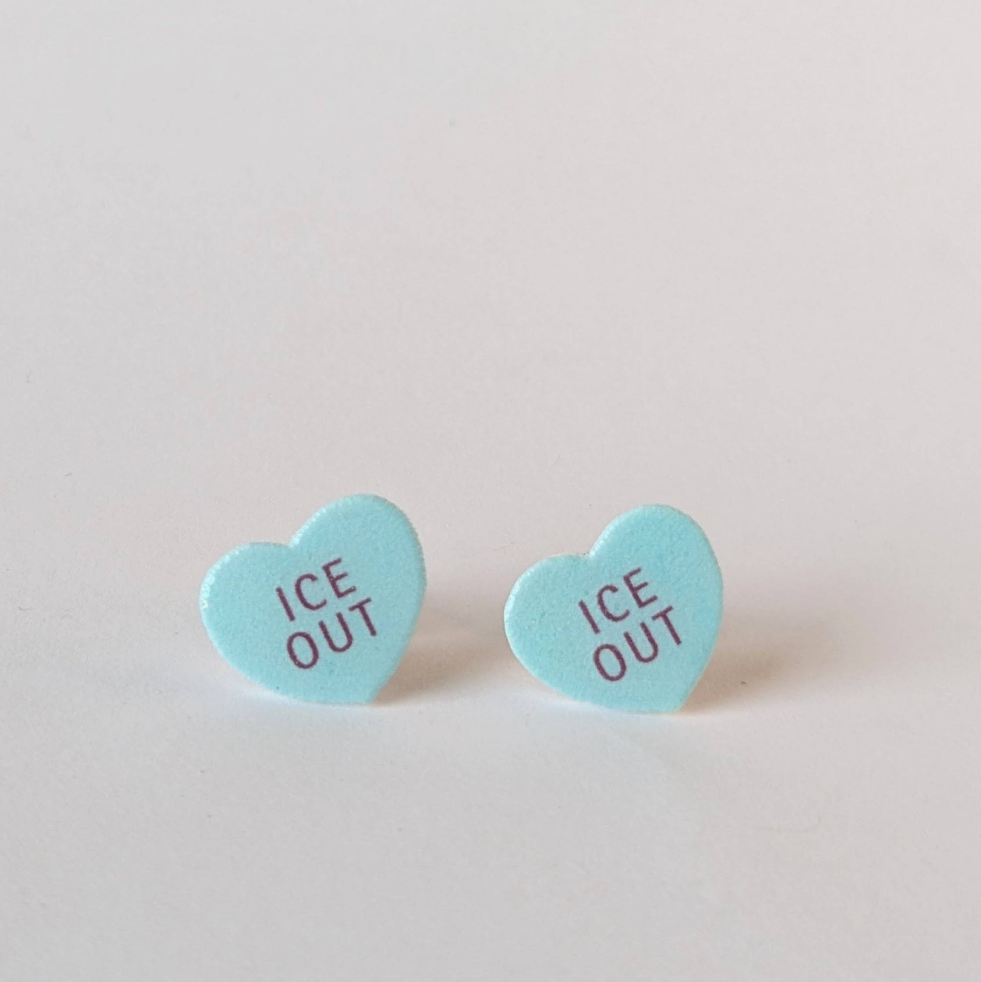 Heart-shaped 'ICE OUT' earrings on a light gray background