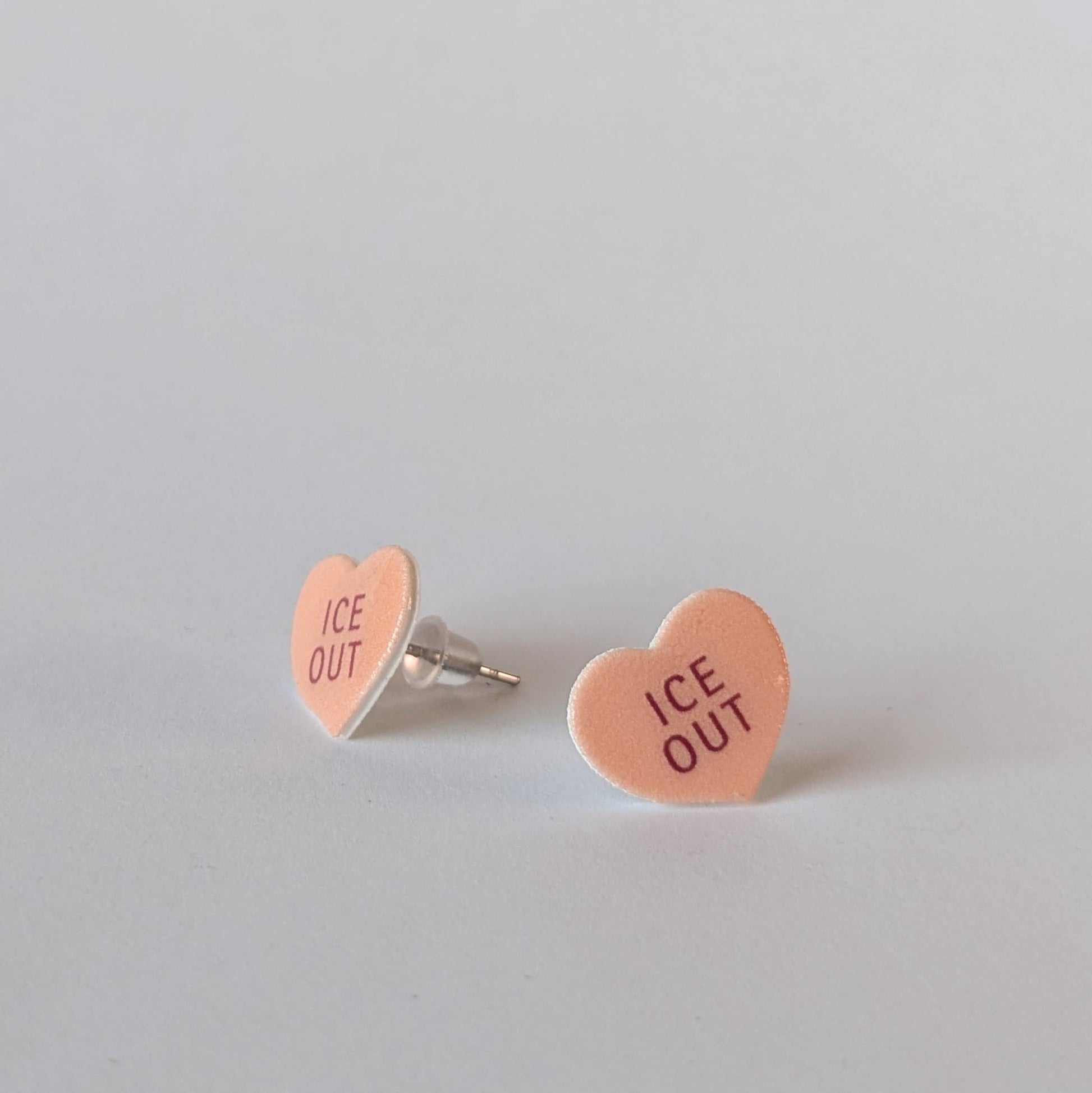 Heart-shaped earrings with 'ICE OUT' text on a light gray background