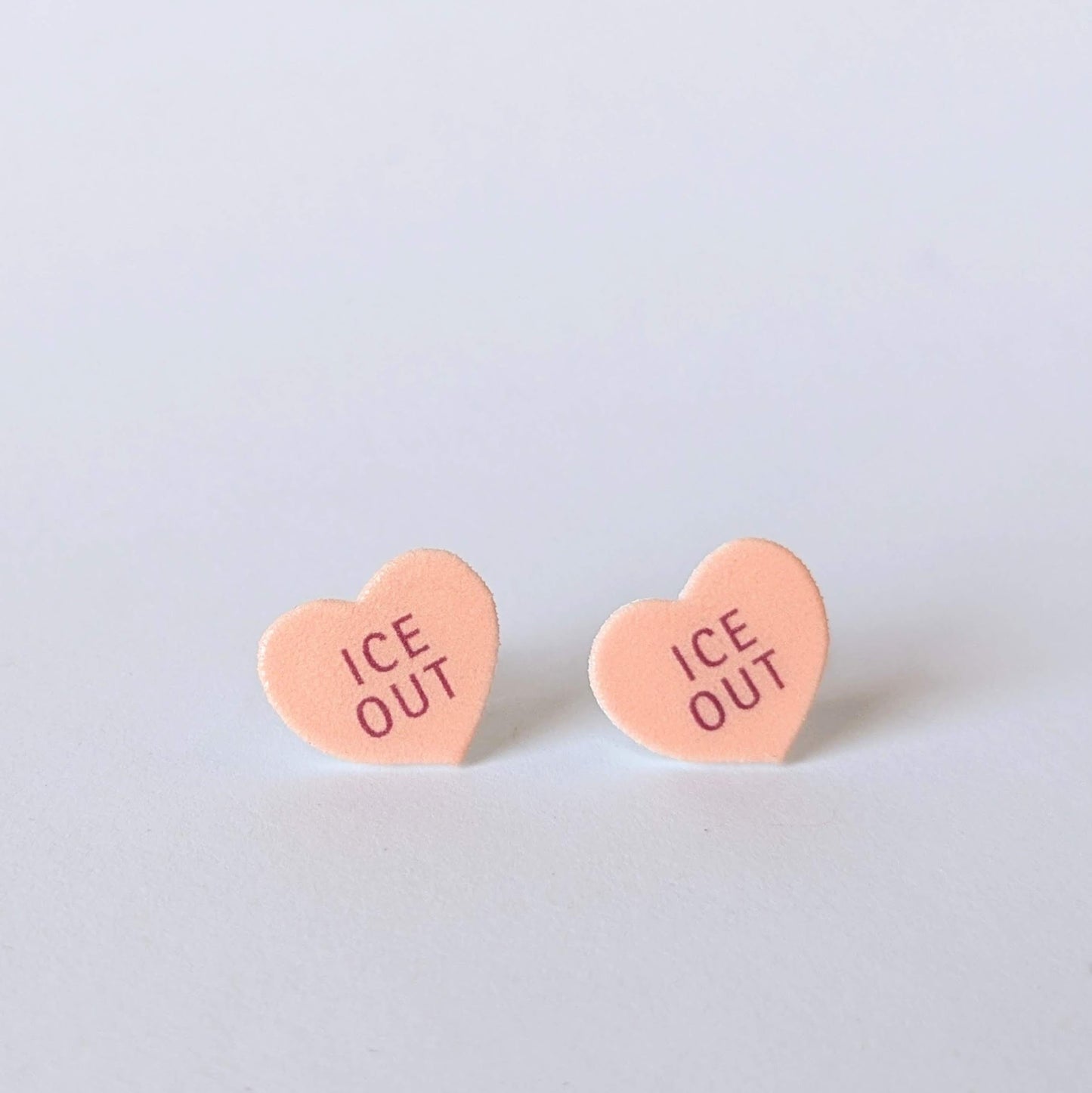 Heart-shaped earrings with 'ICE OUT' text on a light gray background