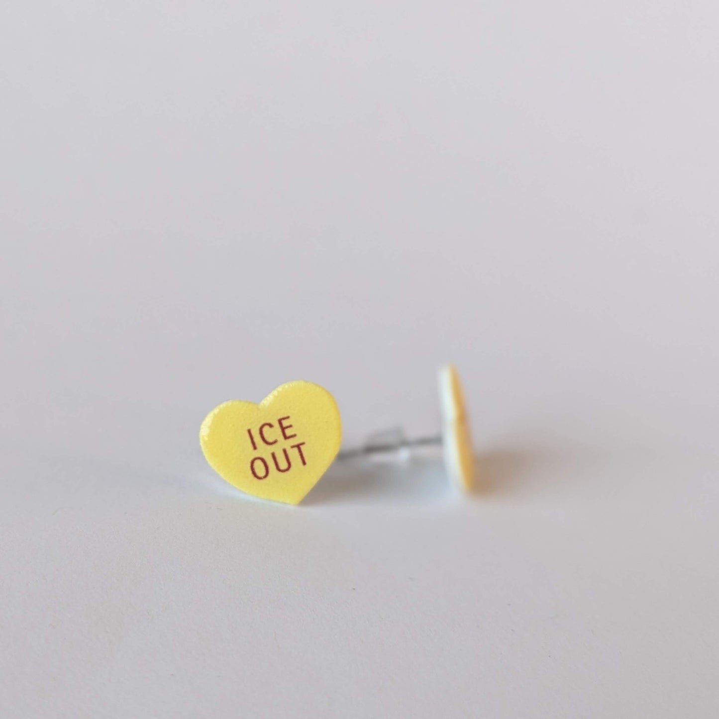 Heart-shaped yellow earring with 'ICE OUT' text on a light gray background