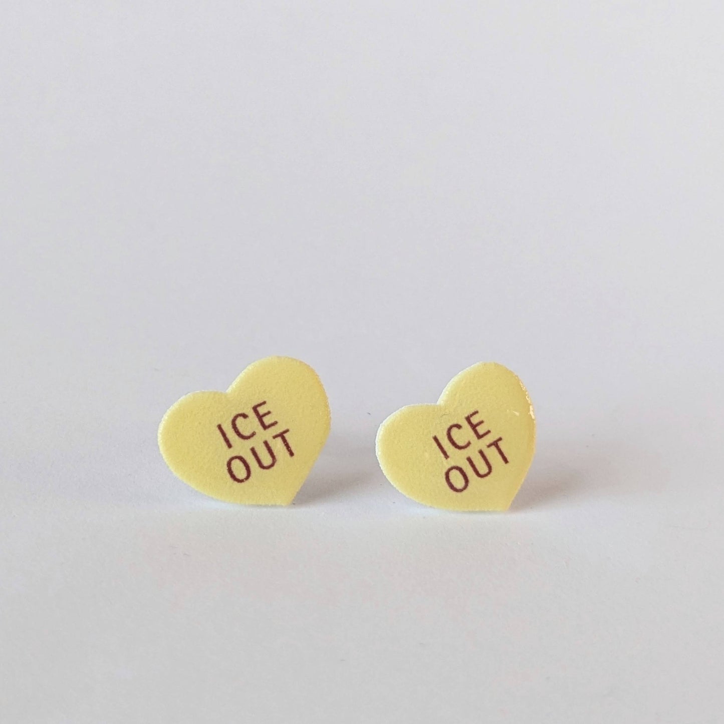 Heart-shaped 'ICE OUT' earrings on a light gray background
