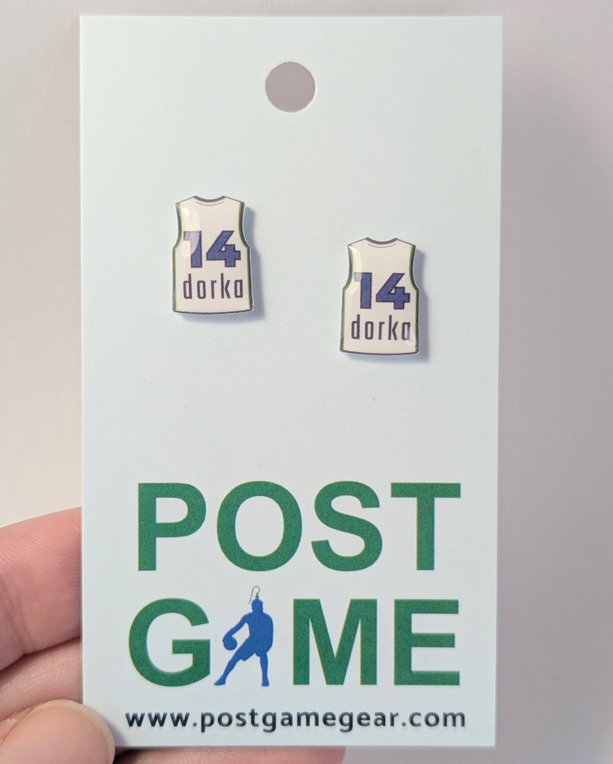 A pair of earrings shaped like basketball jerseys with the number 14 and the name 'dorka' are displayed on a white backing card. The backing card features the green and blue text 'POST GAME' and the website 'www.