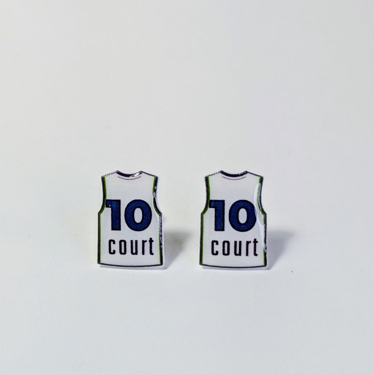 A pair of small earrings shaped like basketball jerseys, each printed with the number 10 and the word 'court' in dark blue on a white background, shown on a plain light gray surface.