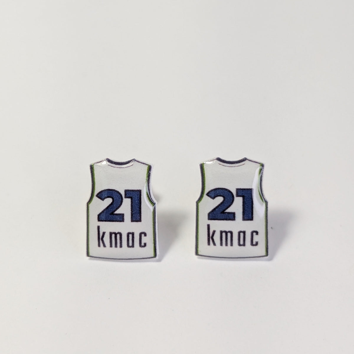 Two small earrings shaped like white basketball jerseys with navy blue numbers 21 and the name 'kmac' printed below, shown on a plain light background.