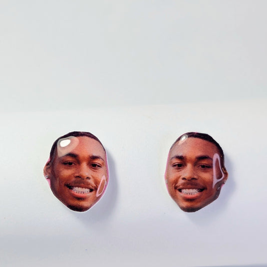 Two oval stud earrings featuring printed photos of a smiling man's face, displayed on a plain white surface.