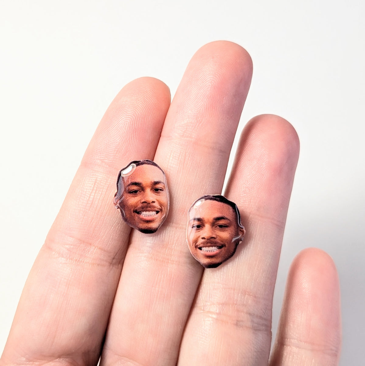 Earrings shaped like a man's face (Justin Jefferson) held against fingers on a light colored background