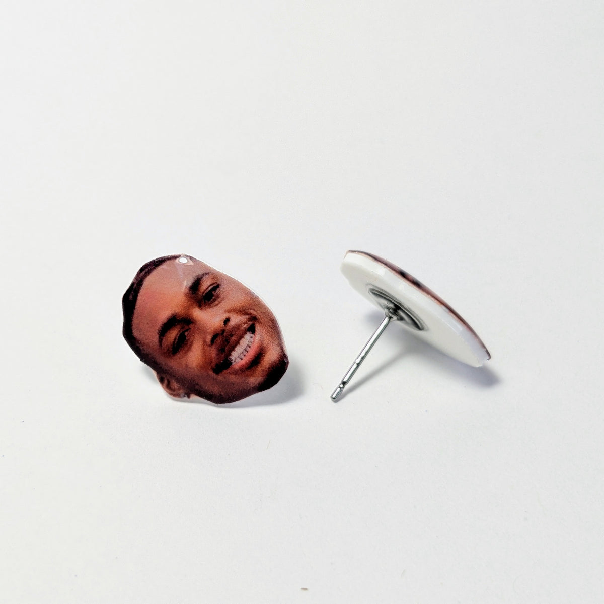 Image of two earrings shaped like the face of Justin Jefferson on a plain light colored background. 