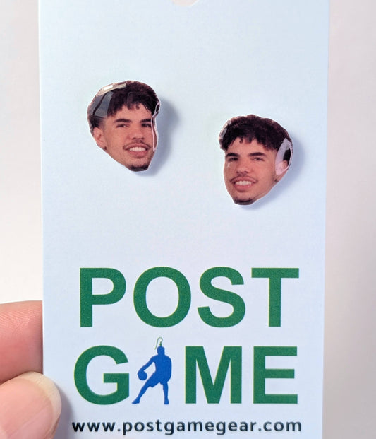 A hand holding a white display card featuring two portrait earrings of Lamelo Ball's face, with the text 'POST GAME' and 'www.postgamegear.