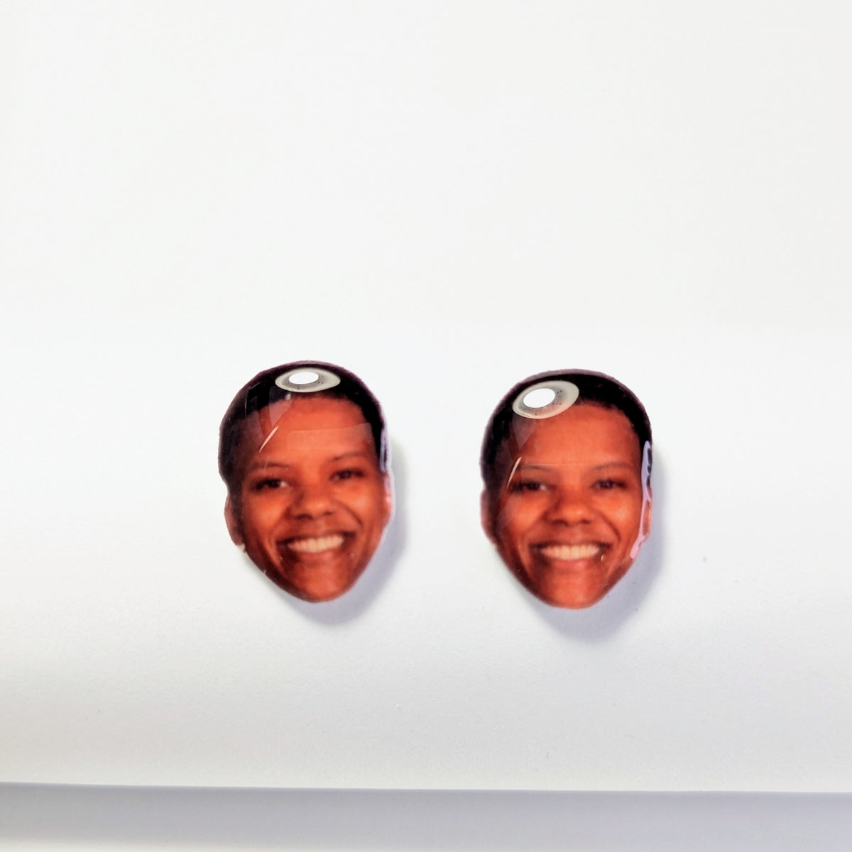 A pair of oval stud earrings featuring a printed photo of a smiling woman with short dark hair, displayed on a plain white background.