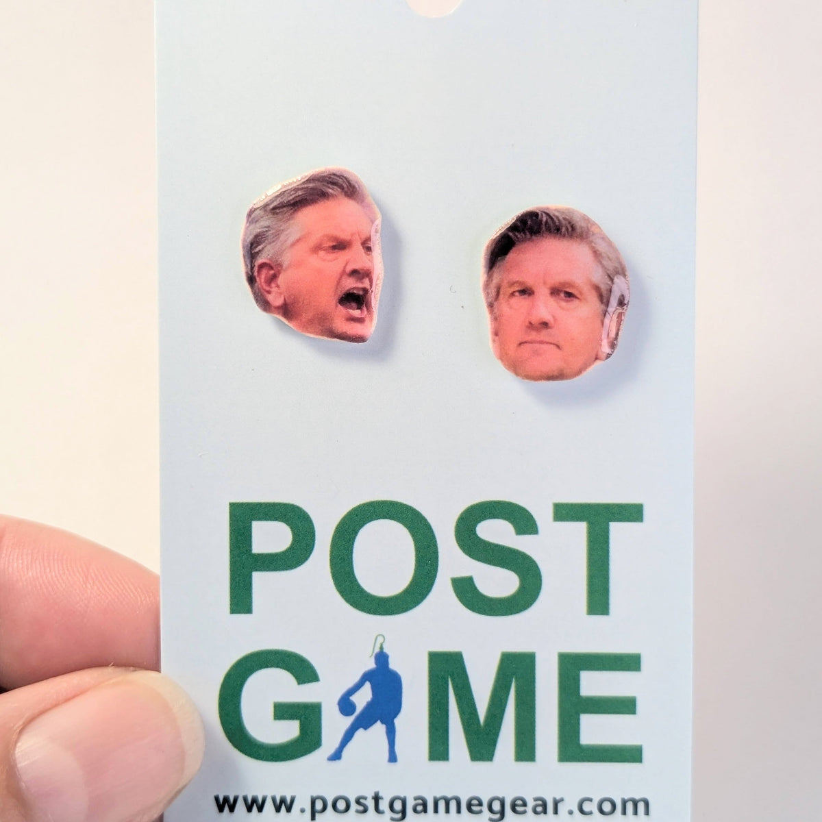 A hand holding a light blue card featuring two die-cut  portraits of a man, above the green text 'POST GAME' and the website 'www.postgamegear.