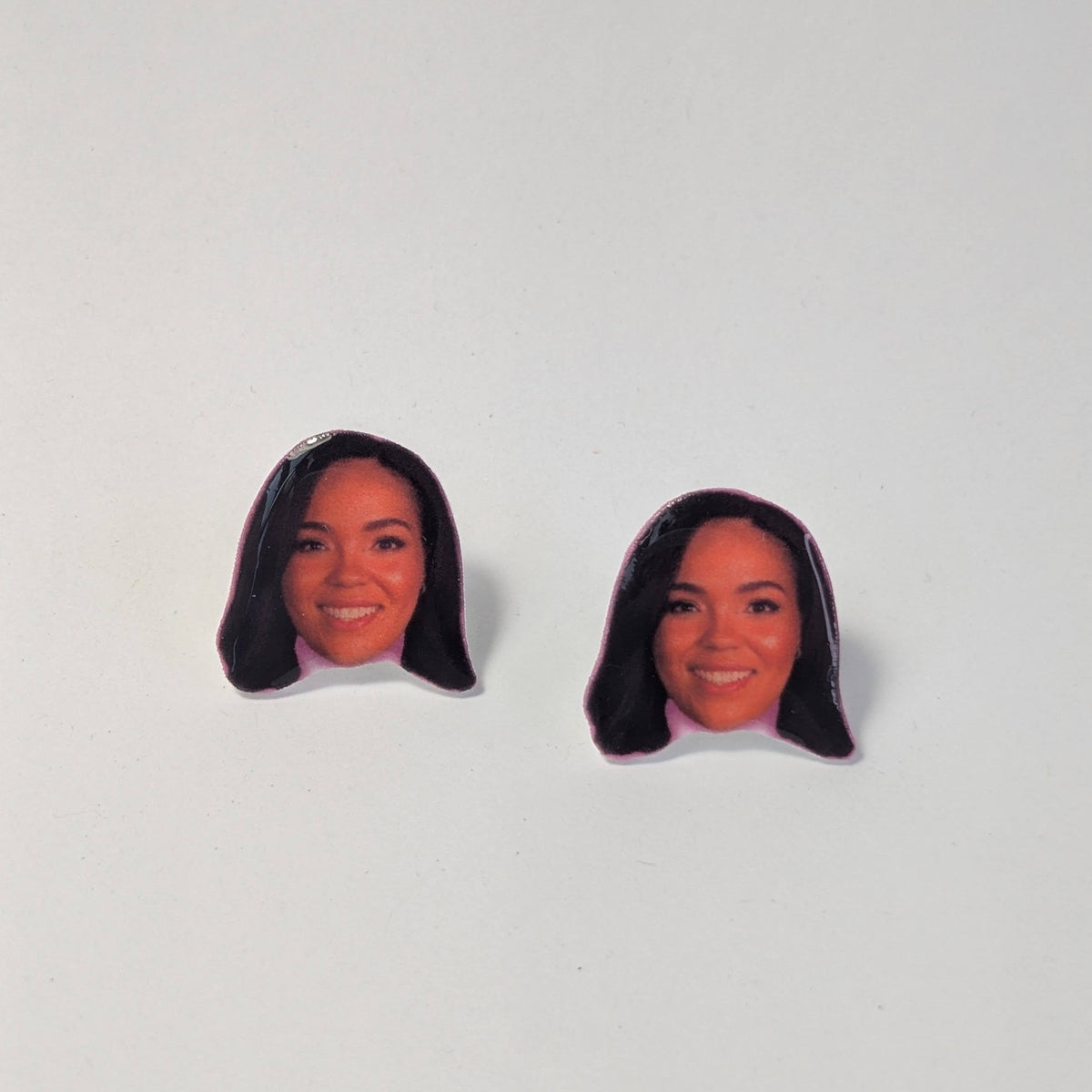 Two small face-shaped earrings with printed portraits of a smiling woman with dark hair, shown on a plain light background.