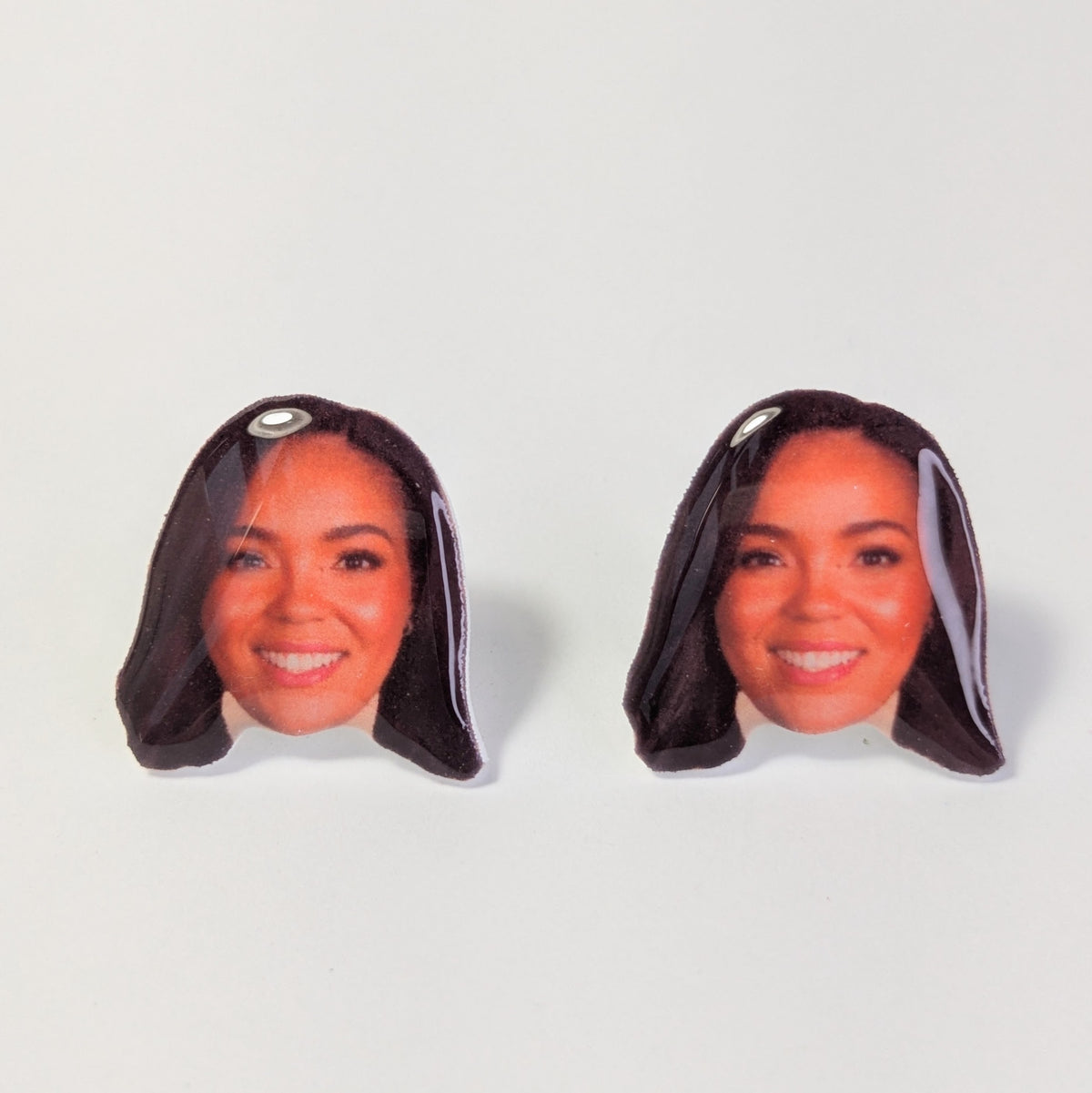 A pair of novelty stud earrings shaped like a woman's head with dark hair, displayed on a clean white background.