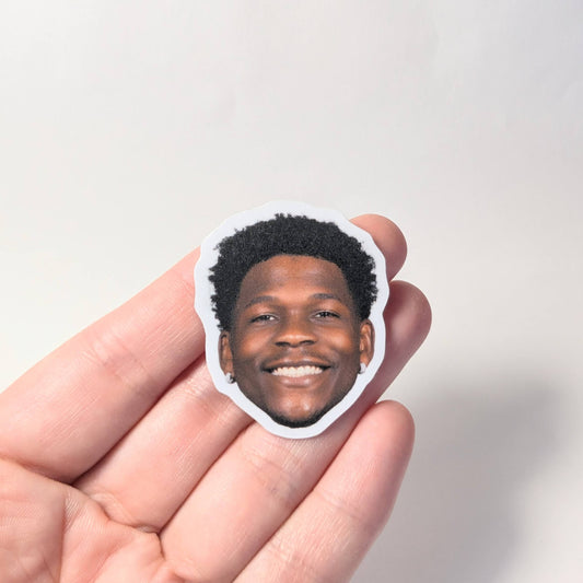 Hand holding a sticker with a person's face on a plain background