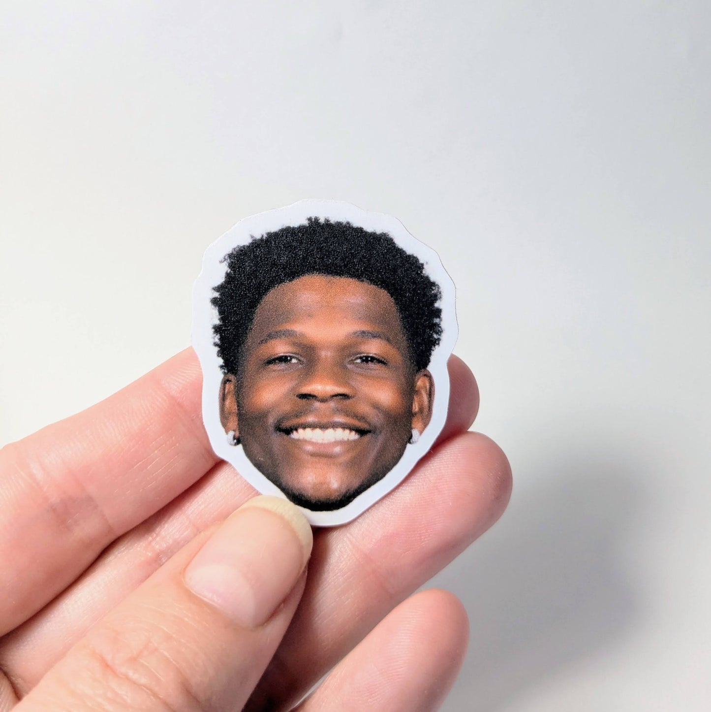 Hand holding a sticker with a smiling person's face against a light gray background