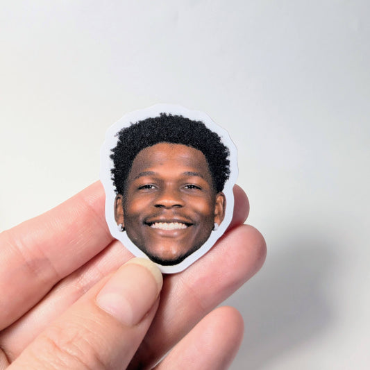 Hand holding a sticker with a smiling person's face against a light gray background
