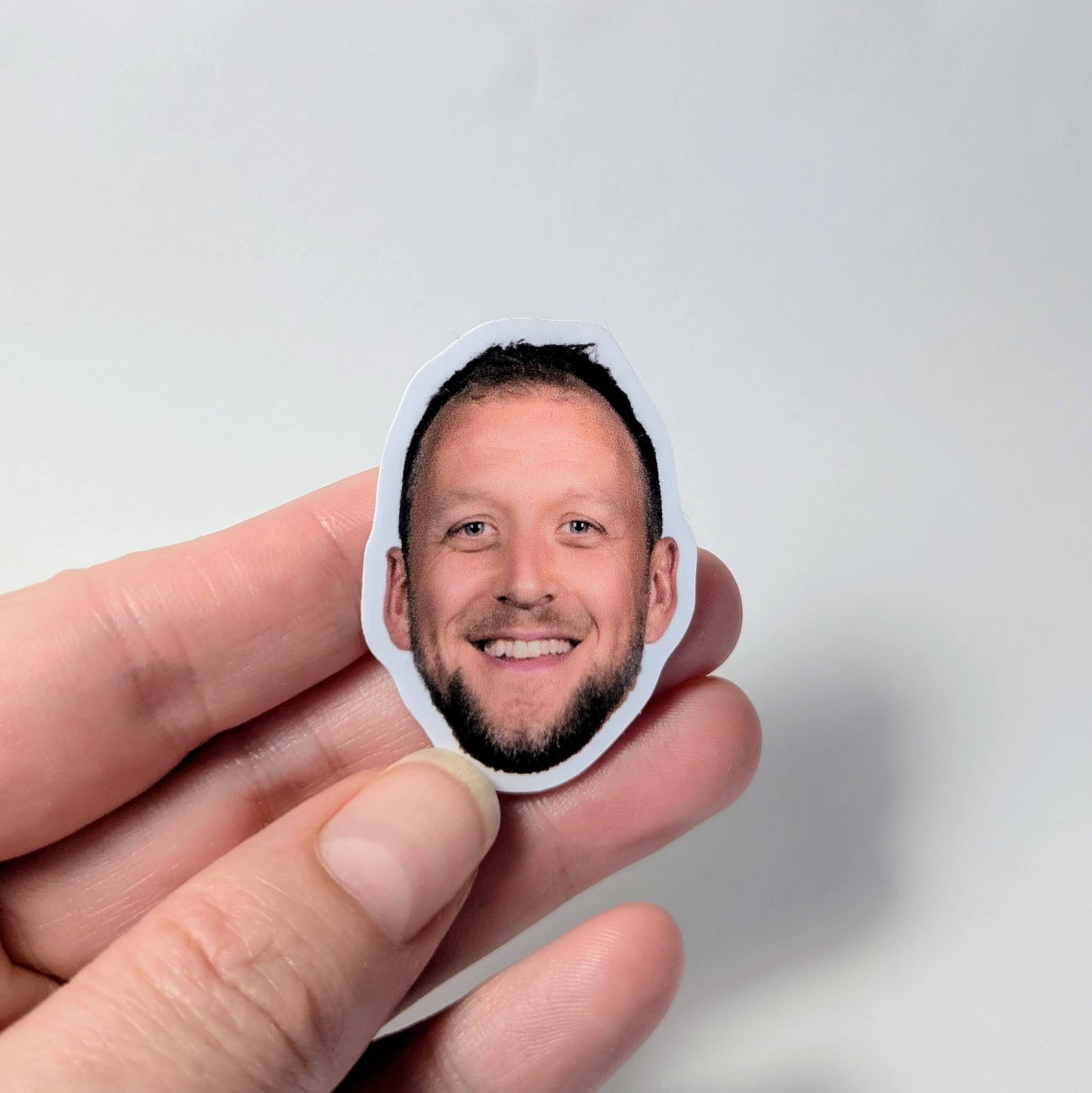 Hand holding a small sticker with a the face of Joe Ingles against a light gray background