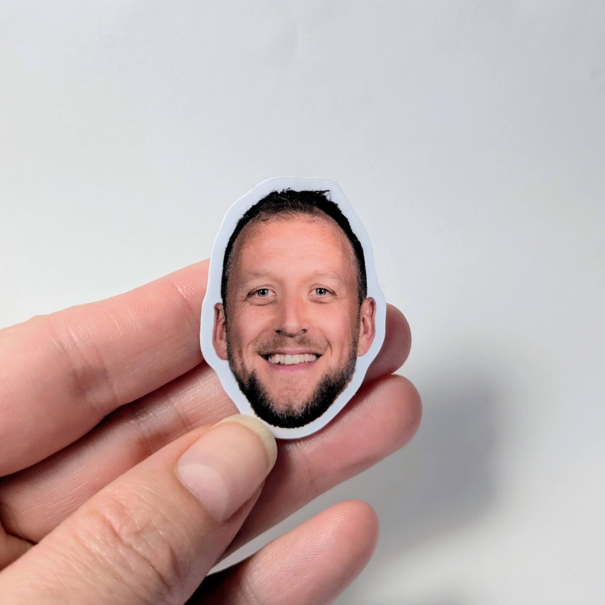 Hand holding a small sticker with a the face of Joe Ingles against a light gray background