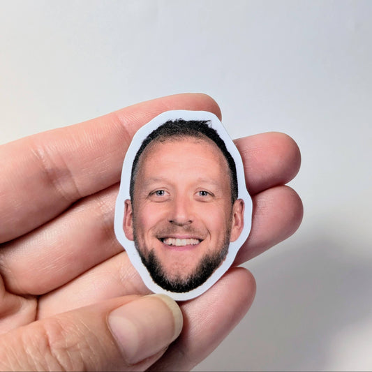 Hand holding a small cutout of a person's face against a light gray background