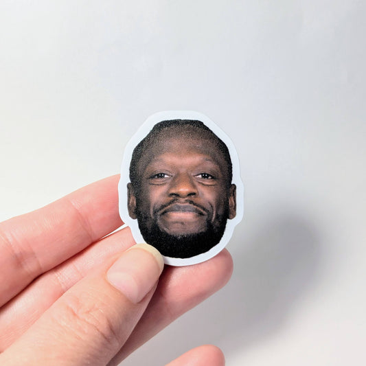 Hand holding a sticker with a person's face against a light gray background