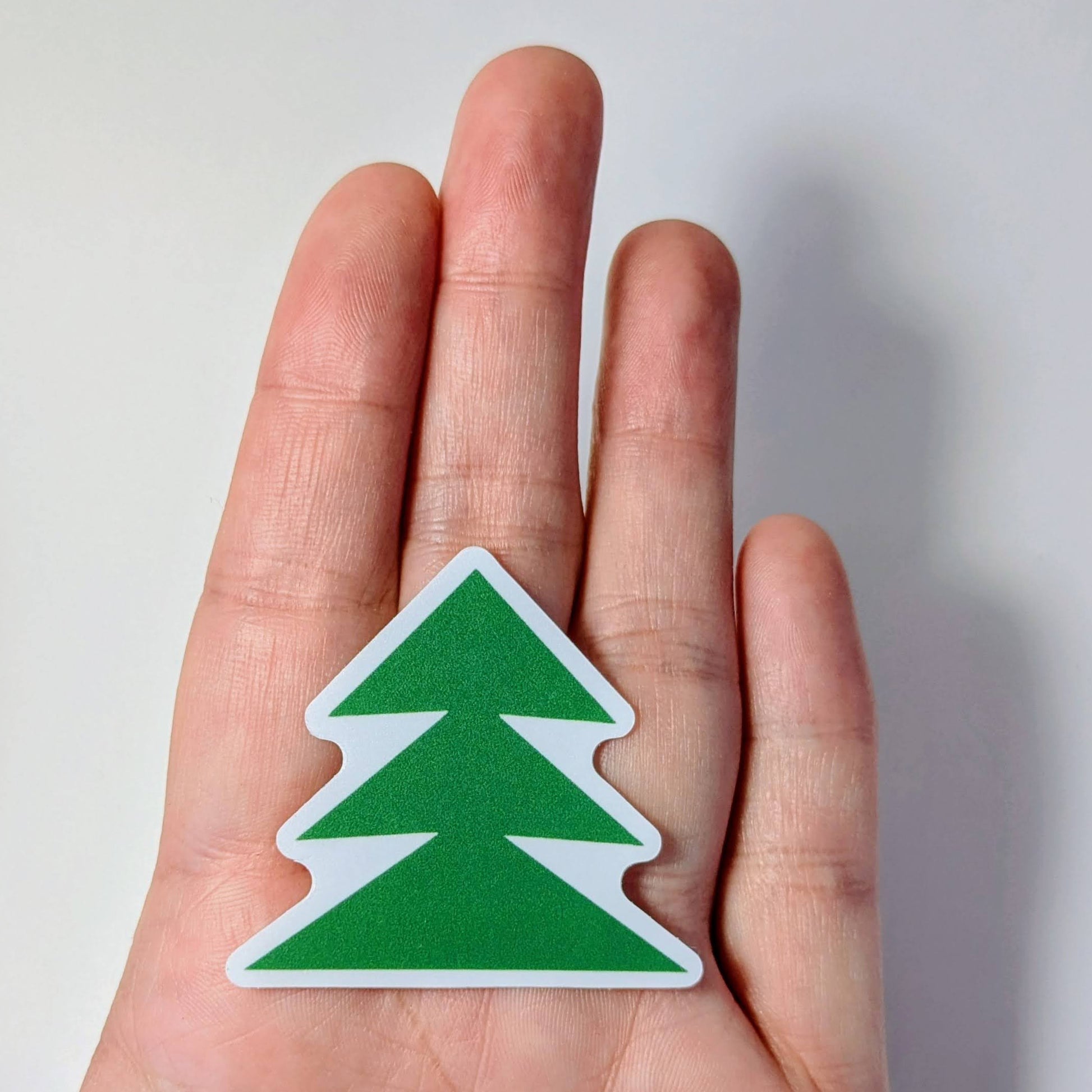 Green and white tree-shaped sticker held in a hand against a light background