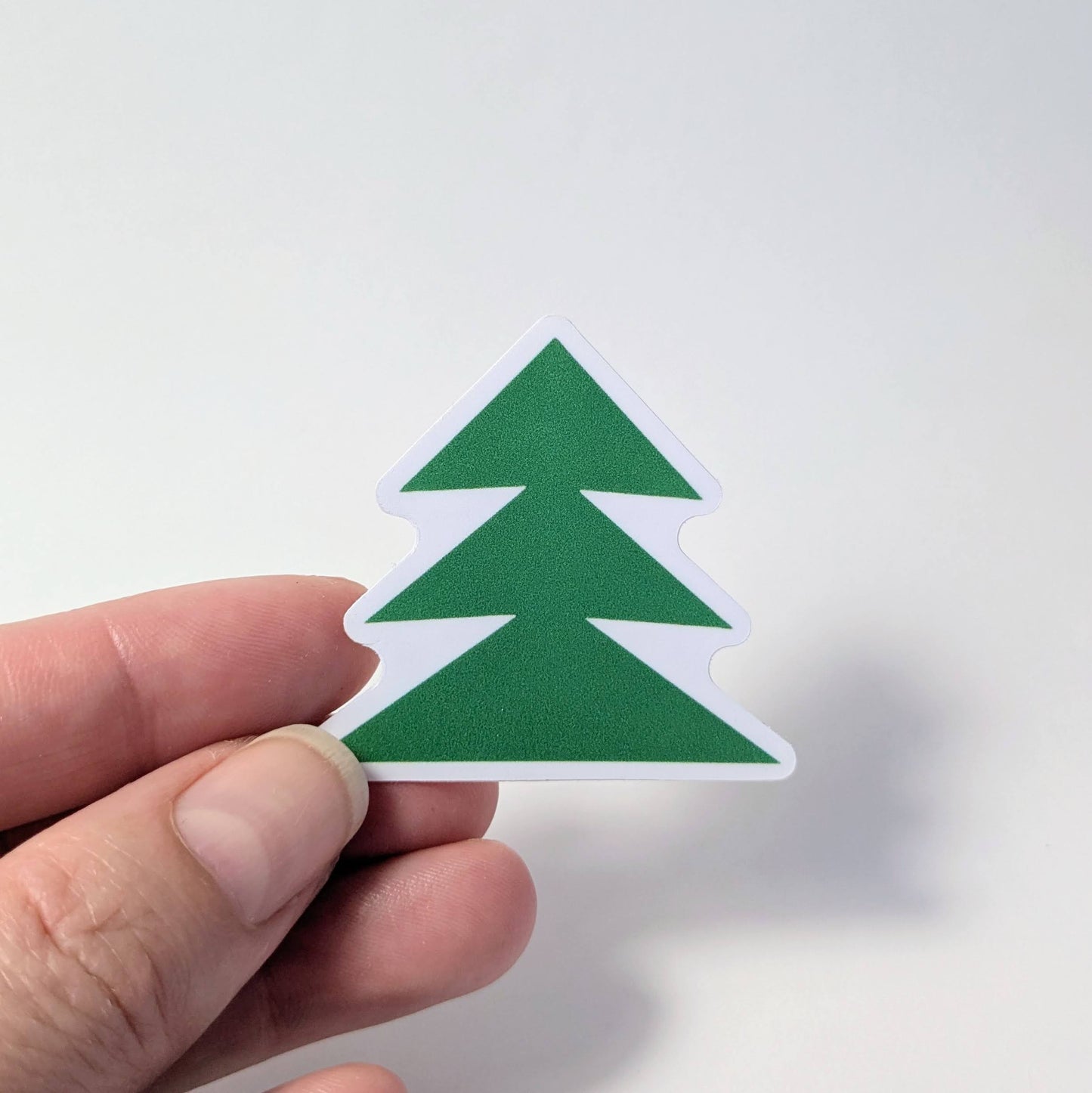 Hand holding a green tree-shaped sticker against a white background