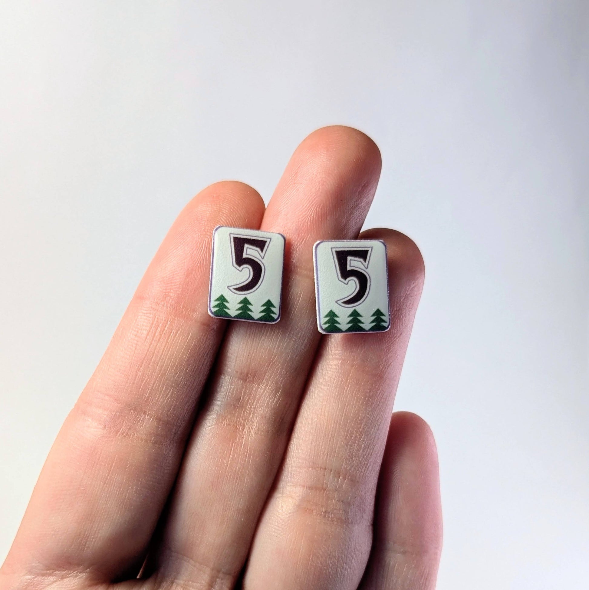 Number 5 earrings held between fingers against a white background
