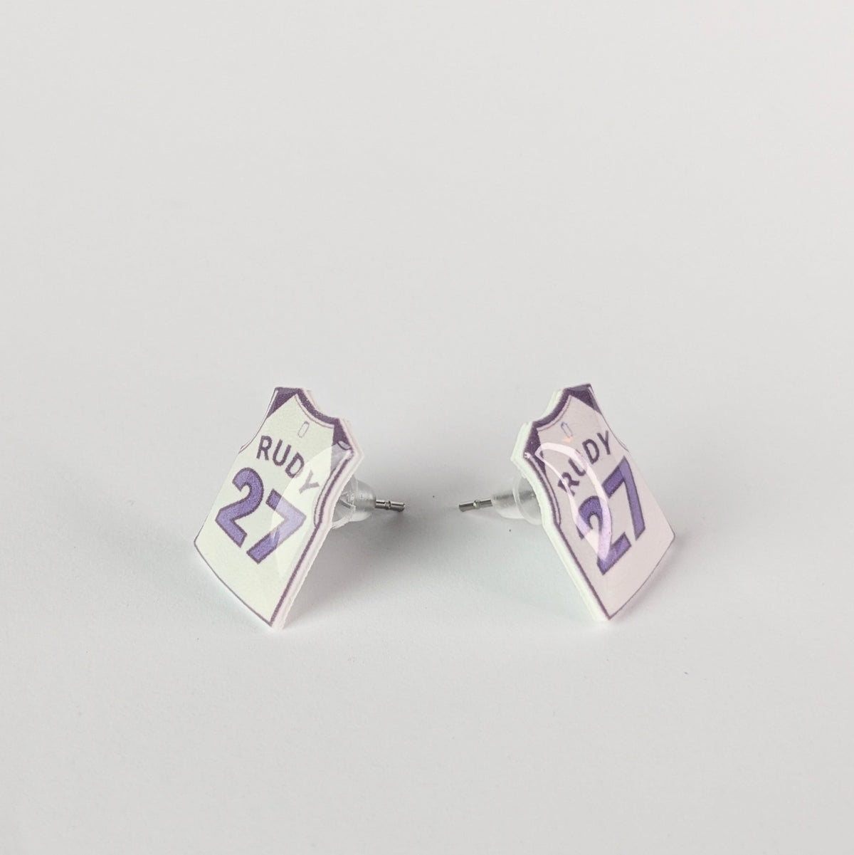 Pair of earrings with 'Rudy 27' design on a light gray background
