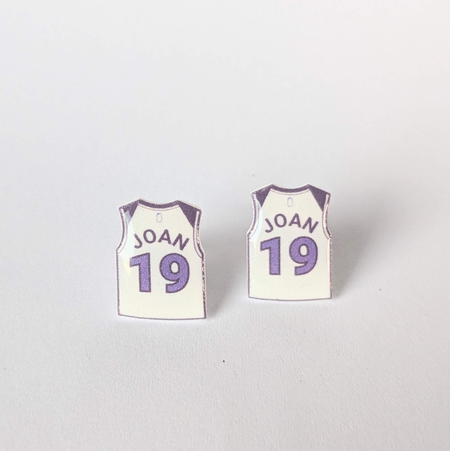 Pair of earrings shaped like basketball jerseys with 'JOAN' and number '19' on a white background