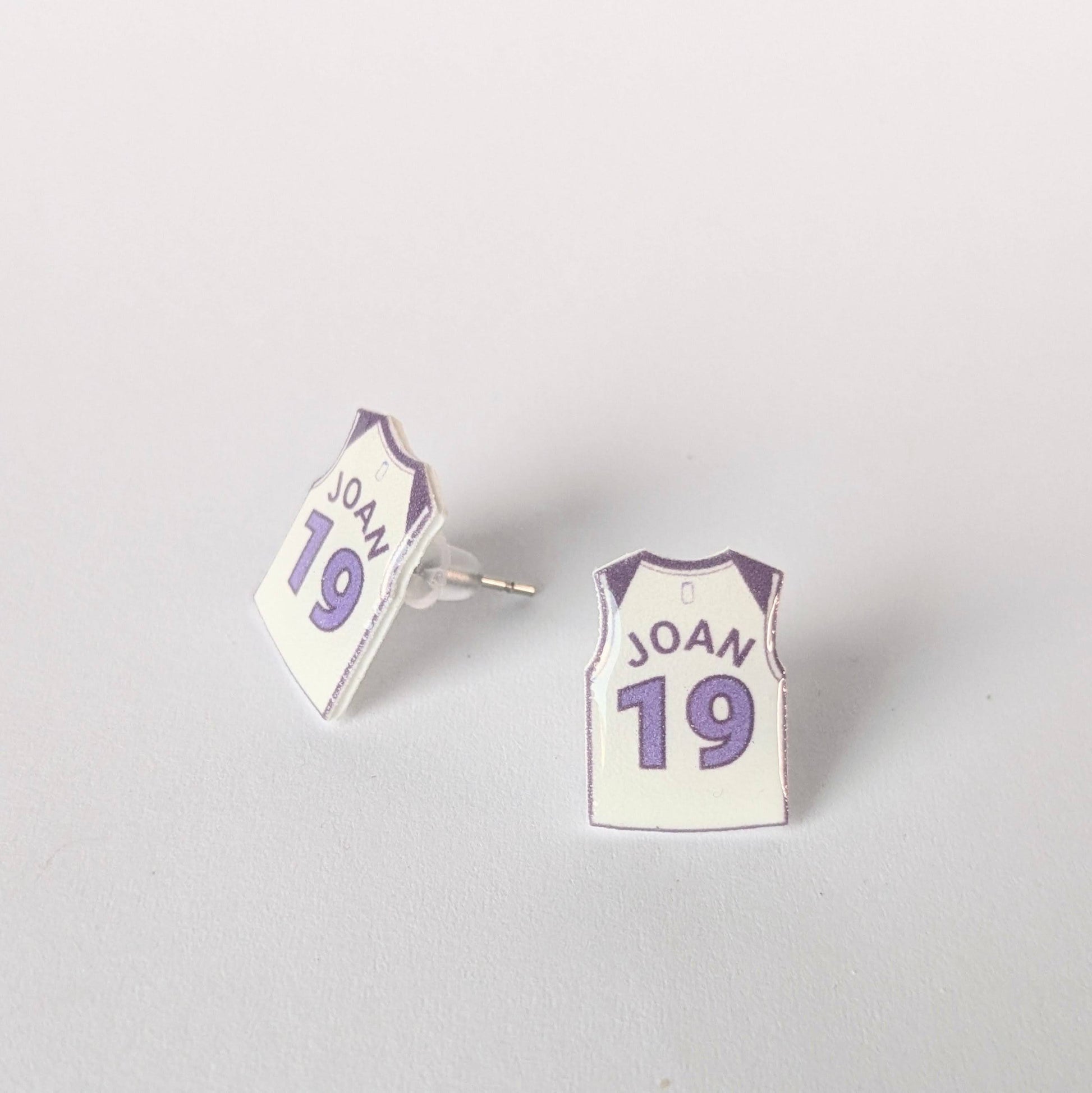 Earrings shaped like mini sports jerseys with 'JOAN' and number '19' on a light gray background