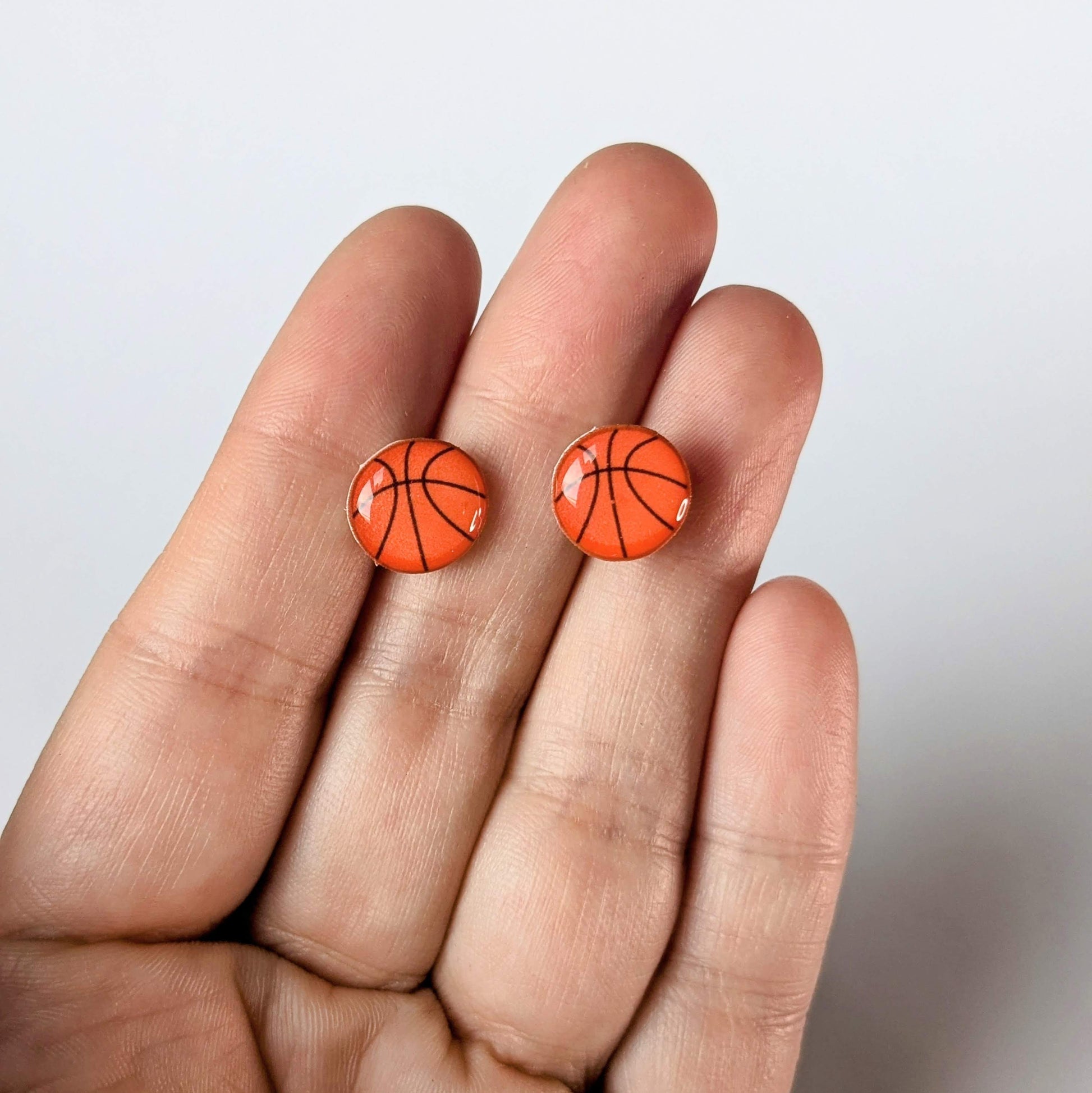Basketball-shaped earrings held between fingers against a light background