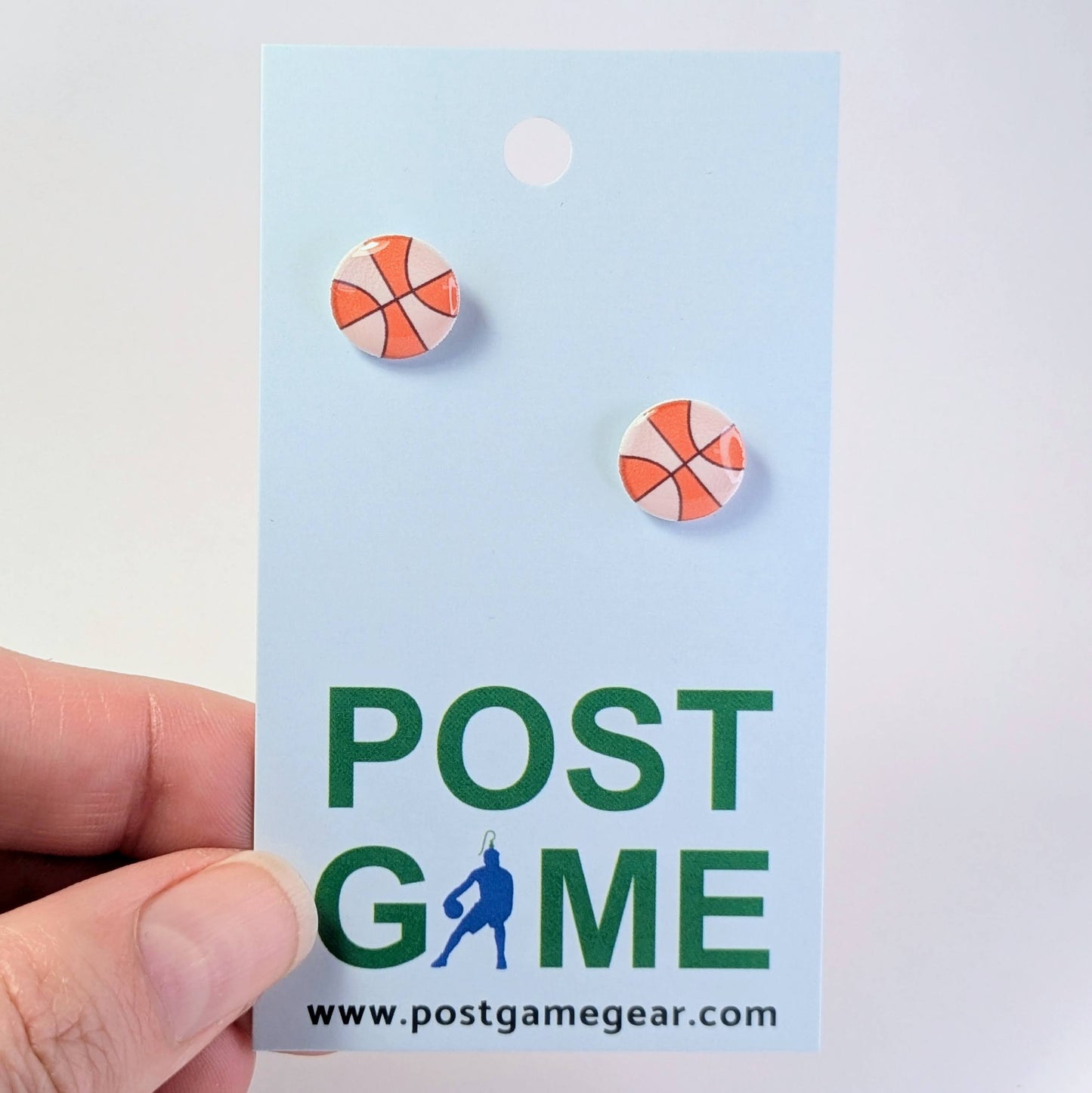 Earrings on a 'POST GAME' branded card held by a hand.