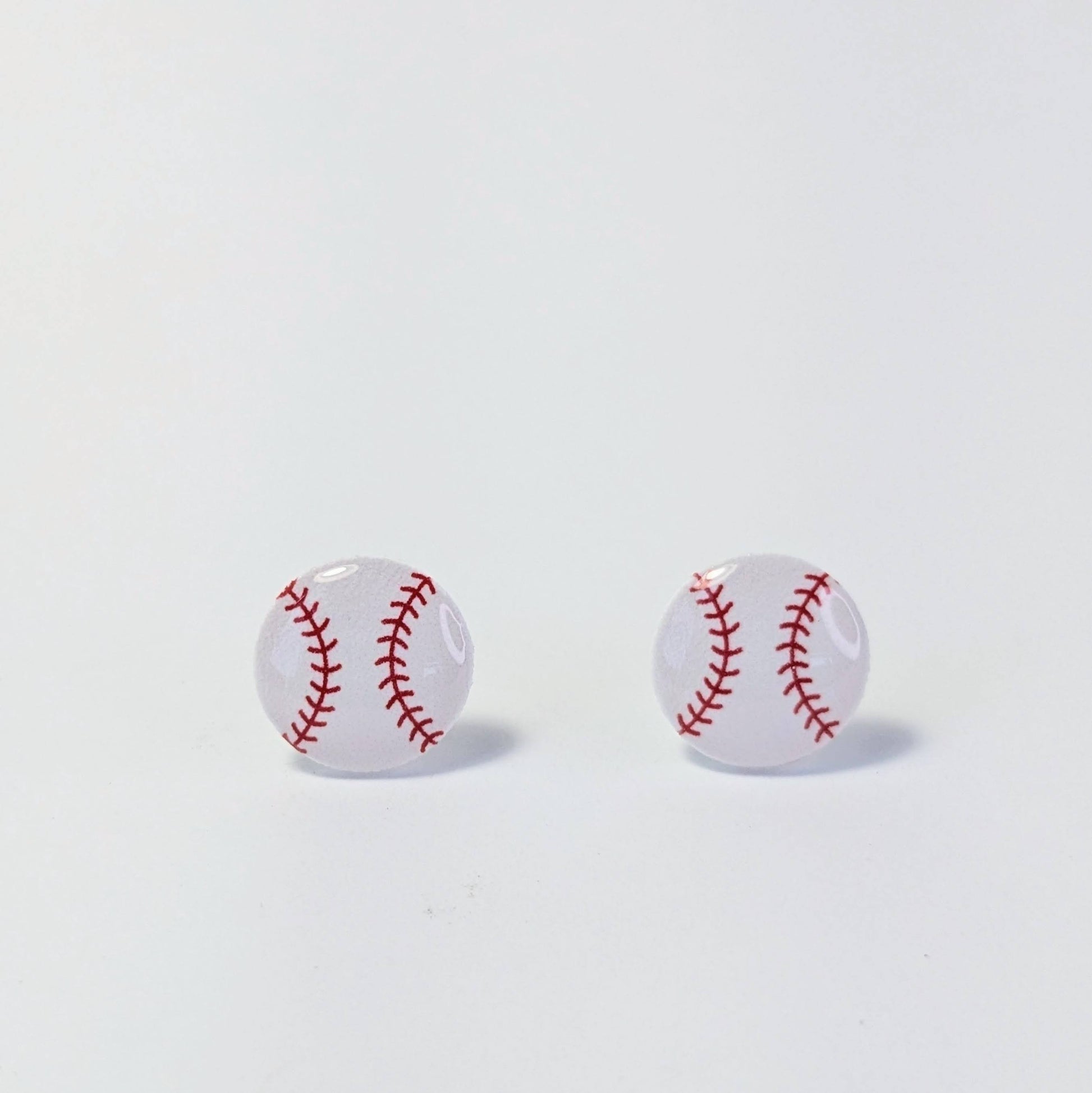 Baseball-shaped earrings with red stitching on a light gray background