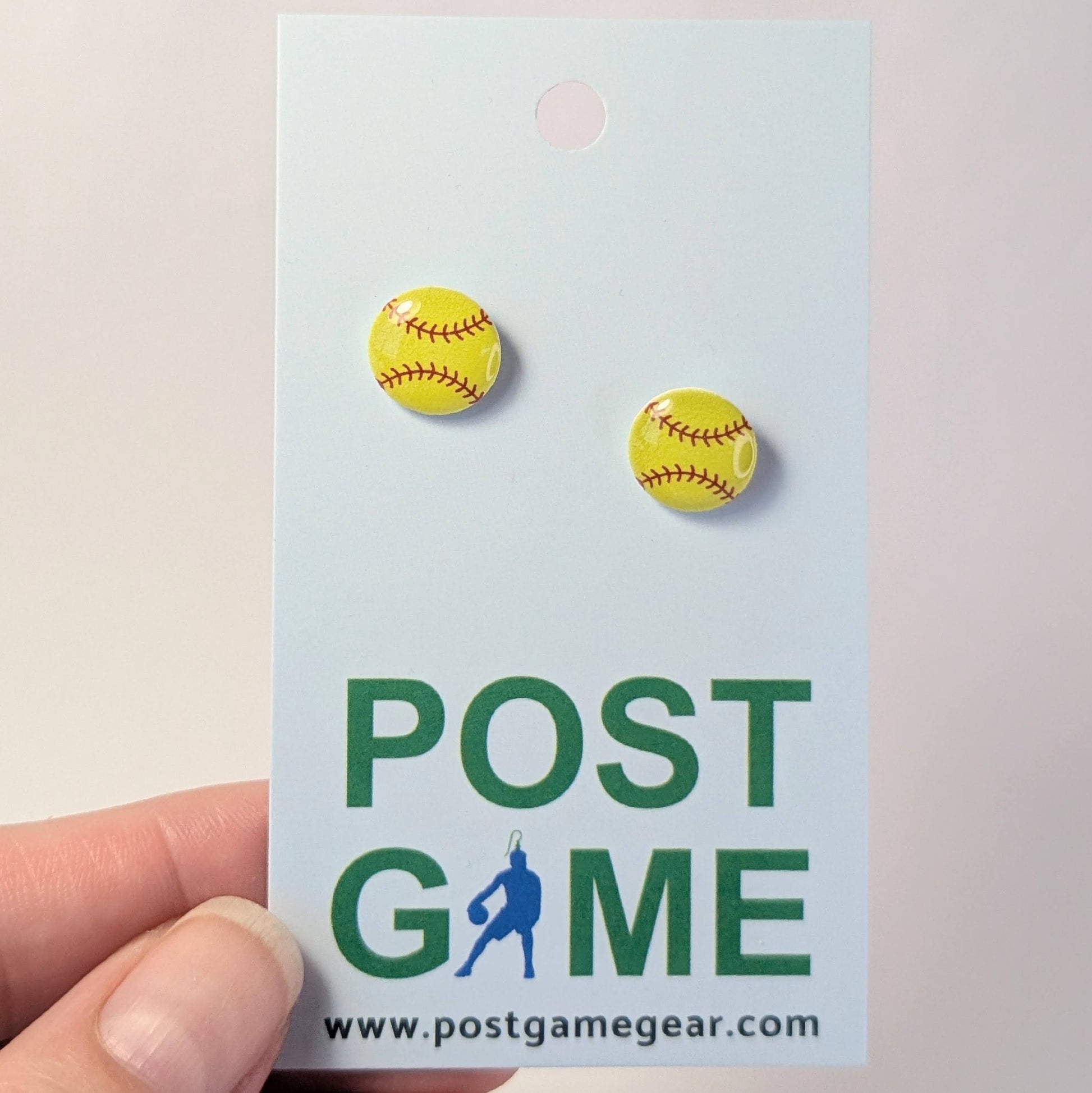 Yellow softball earrings on a 'POST GAME' branded card held by a hand.