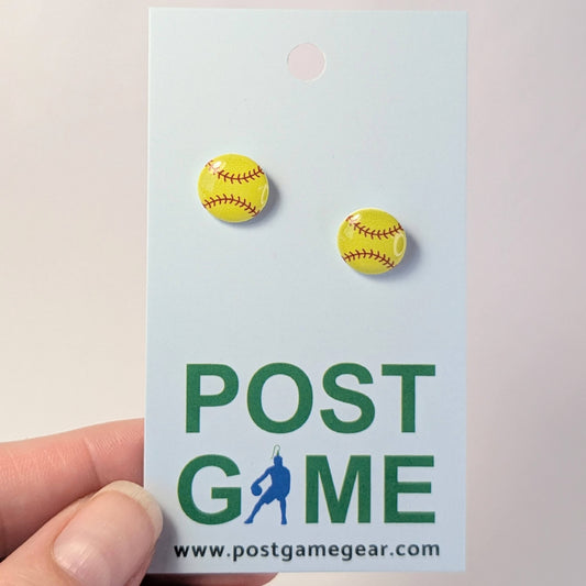 Yellow softball earrings on a 'POST GAME' branded card held by a hand.