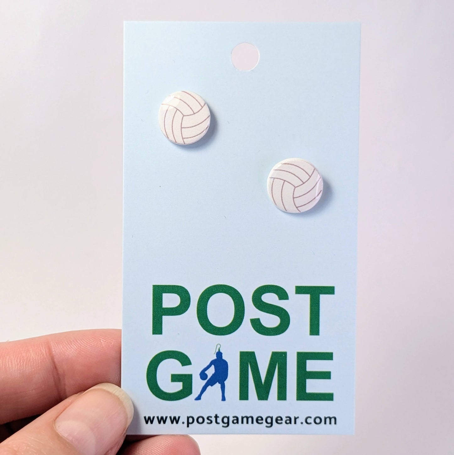 Volleyball-shaped earrings on a 'POST GAME' branded card held by a hand.