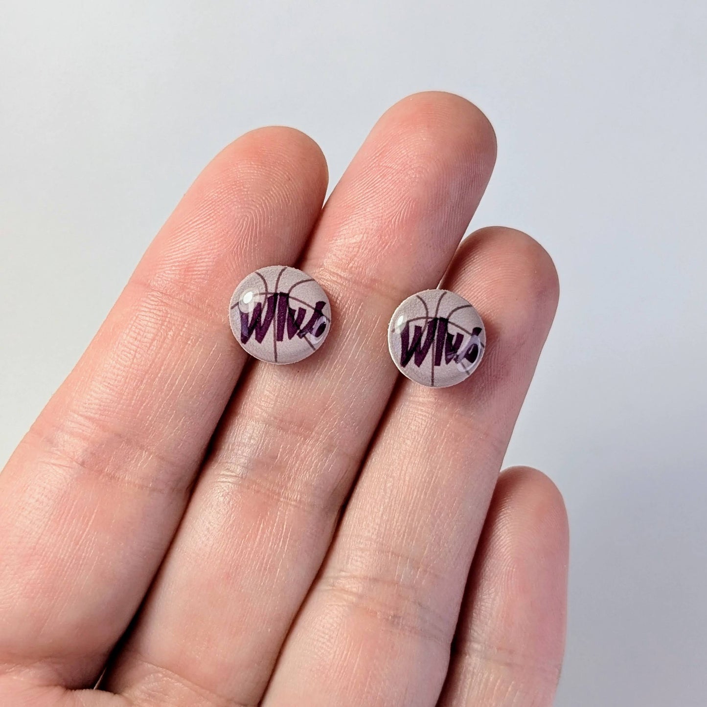 Two round earrings with 'Wlvs' design held between fingers on a light background
