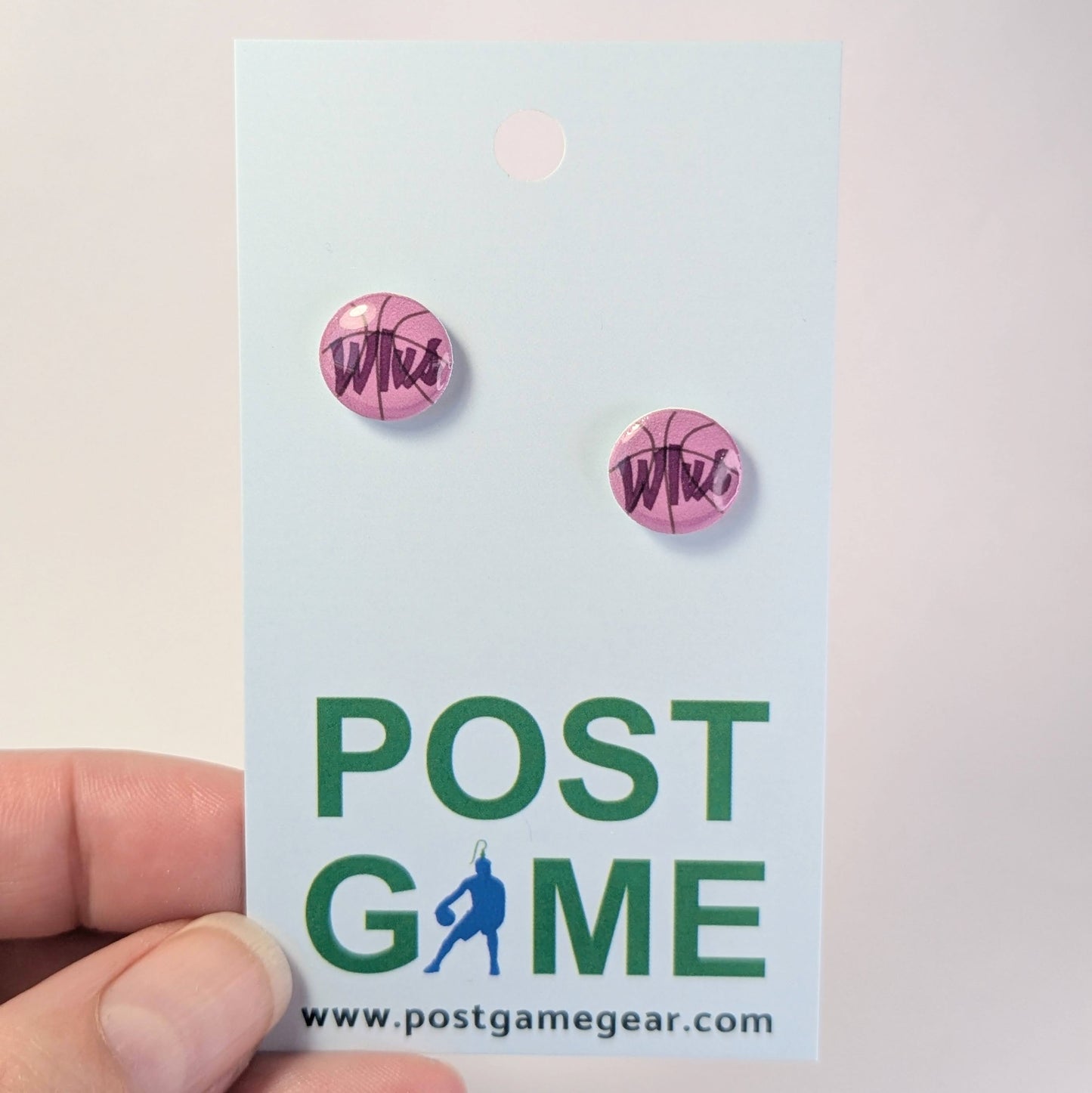 Purple earrings on a 'POST GAME' branded card held by a hand.