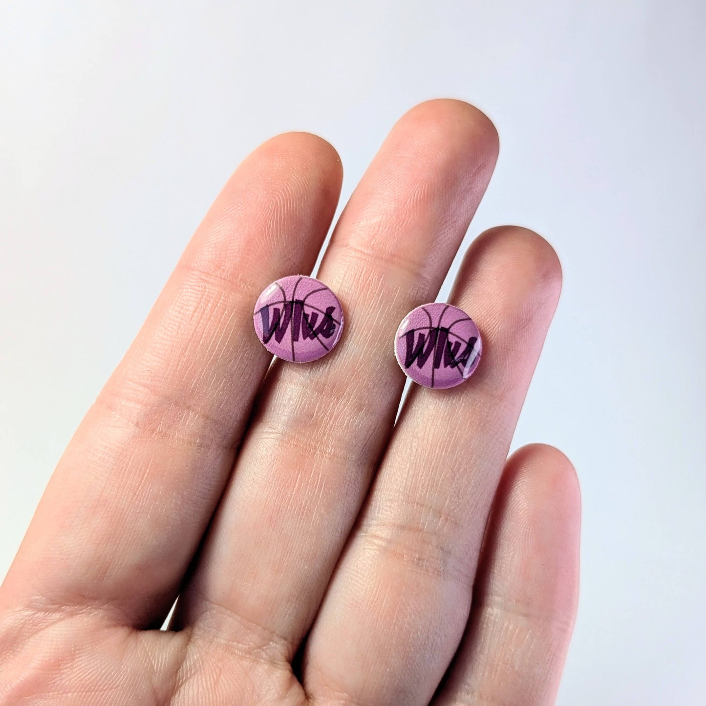 Purple earrings with 'Wlvs' design held between fingers against a light background