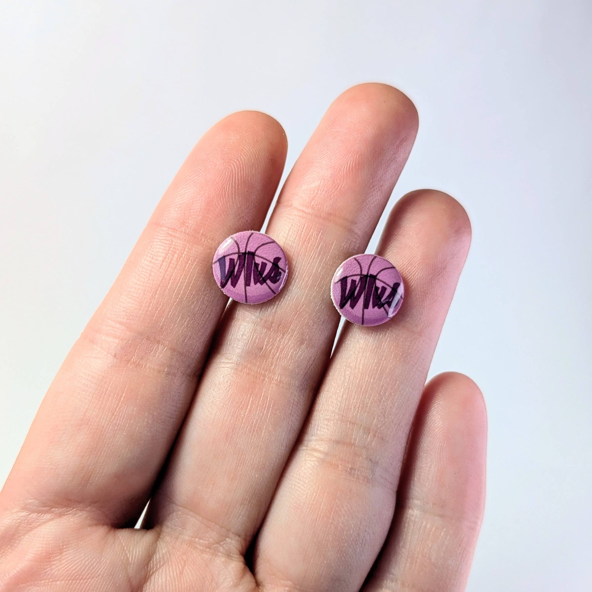 Purple earrings with 'Wlvs' design held between fingers against a light background