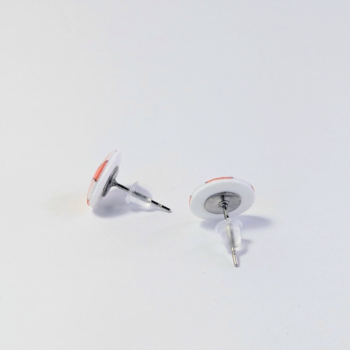 Pair of earrings with white and orange design on a light gray background. Earrings are facing away, showing the metal posts and plastic backs.