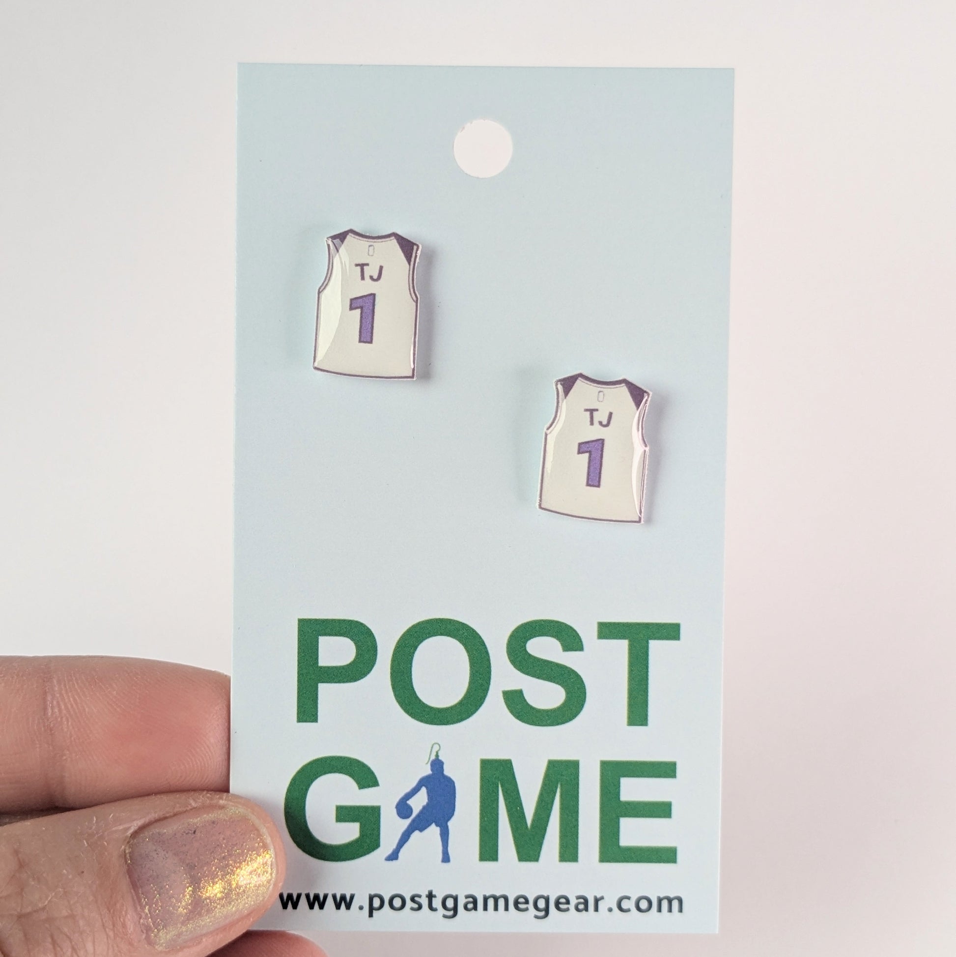 Pair of basketball jerseyearrings on a 'POST GAME' card with a hand holding it.