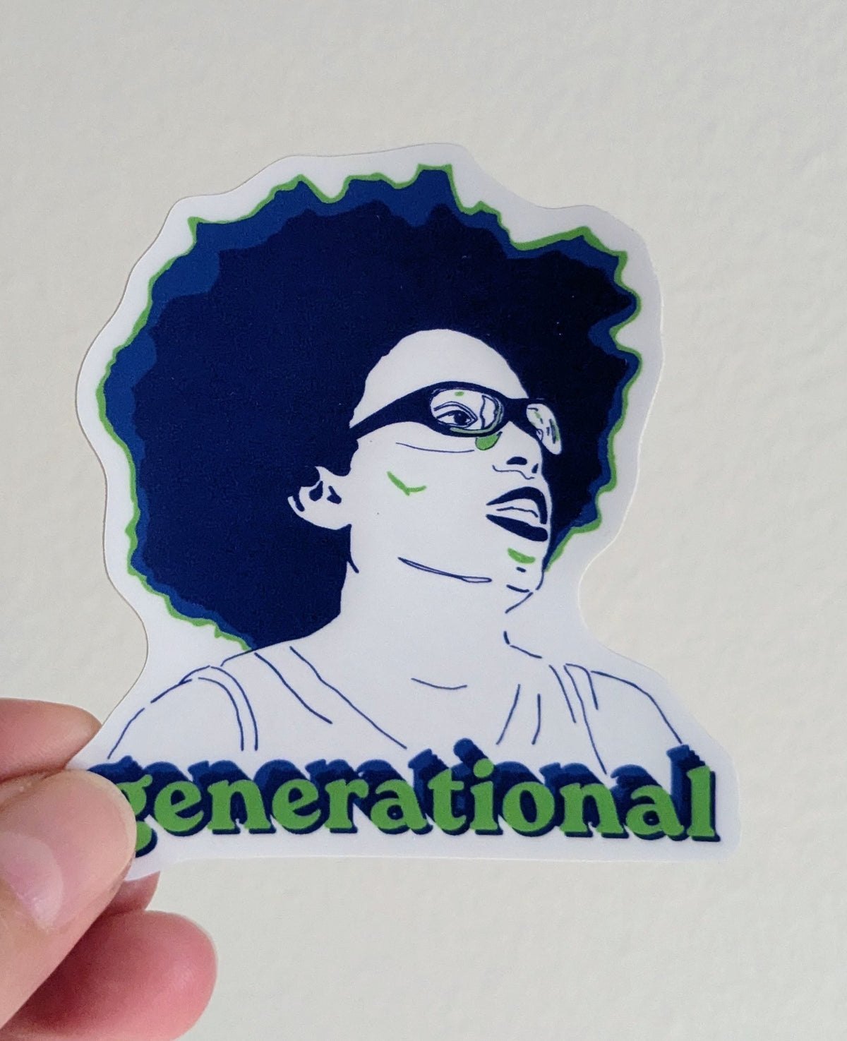 A die-cut sticker held by a hand against a plain off-white background. The sticker features a stylized illustration of a person, (Olivia Miles) with glasses and a dark blue afro, with the word 'generational' in green outlined text across the bottom.