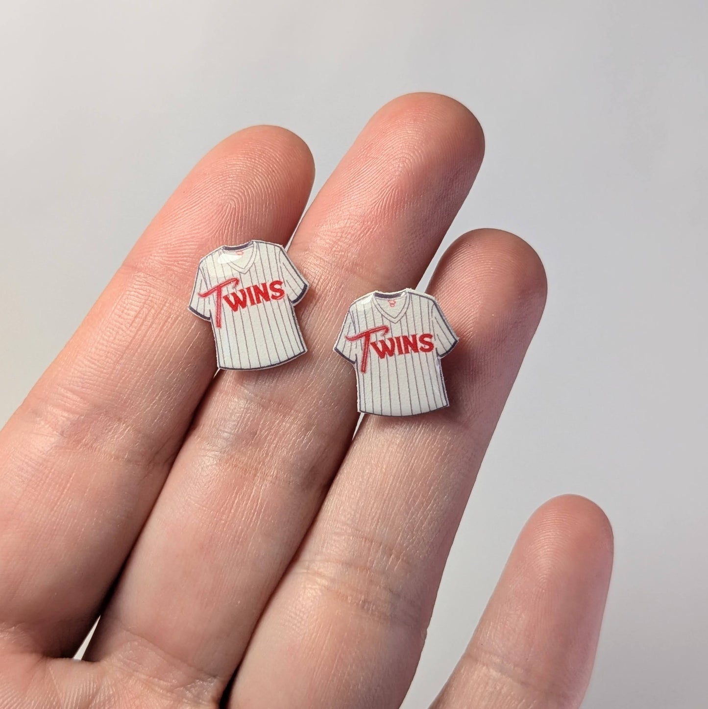 Two small pins shaped like baseball jerseys with 'TWINS' text on a hand against a light gray background.